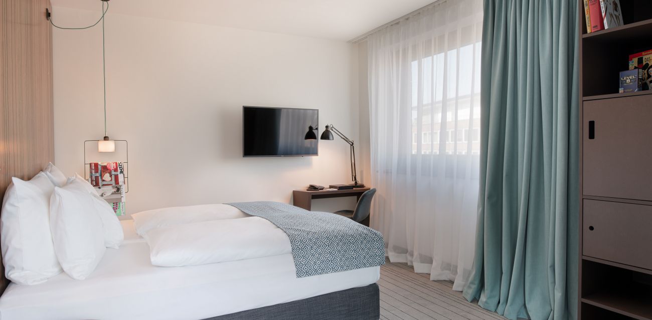 View into wheelchair friendly LARGE room with bed, TV, desk with chair and lamp