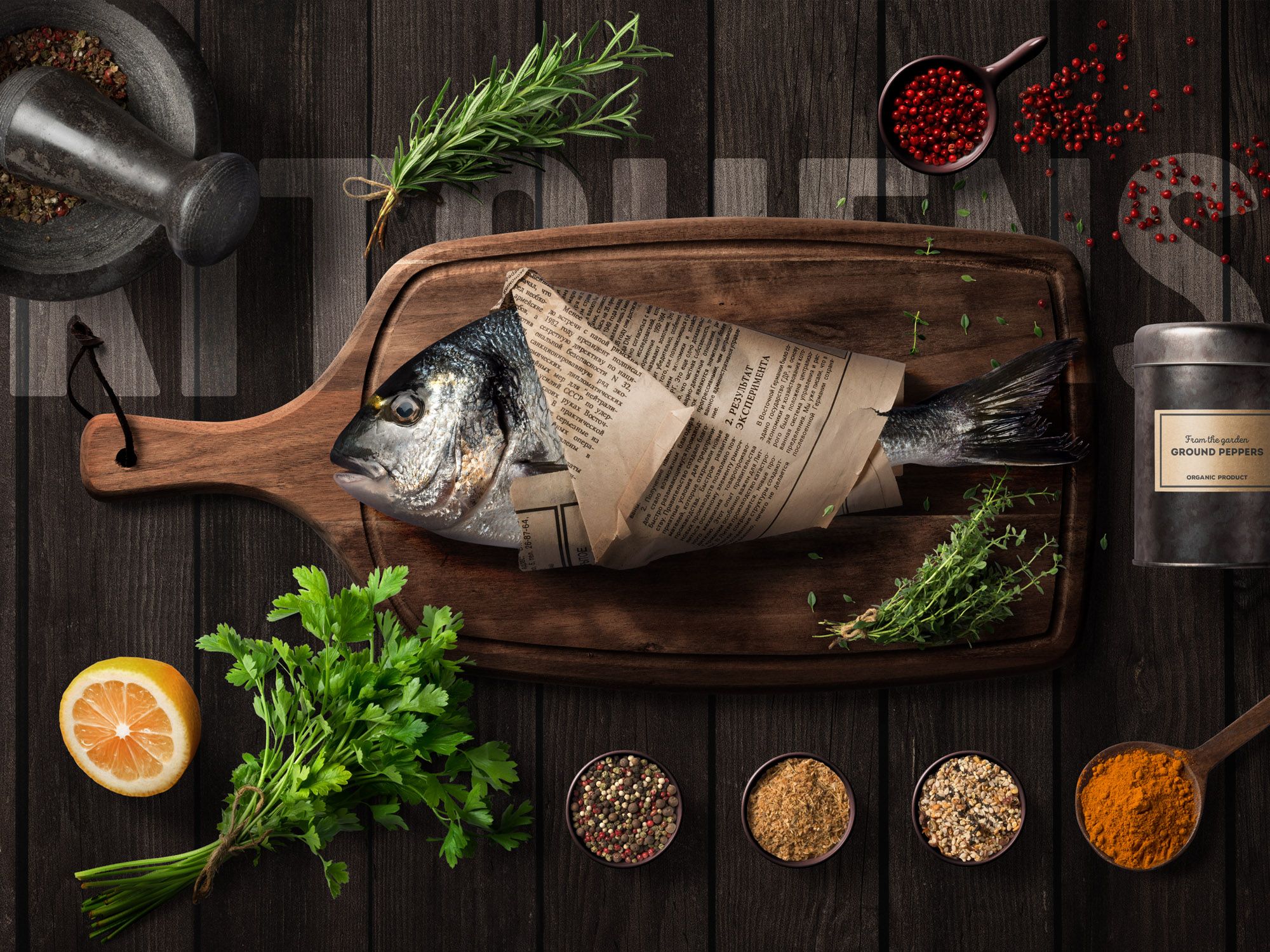 In Zeitung eingepackter Fisch auf Holzbrett, umgeben von Kräutern und Gewürzen, im Restaurant Kitchens 