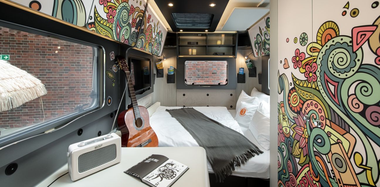 Interior of the camper Hippie Coco with small table, guitar, sleeping area and colorful wall covering 